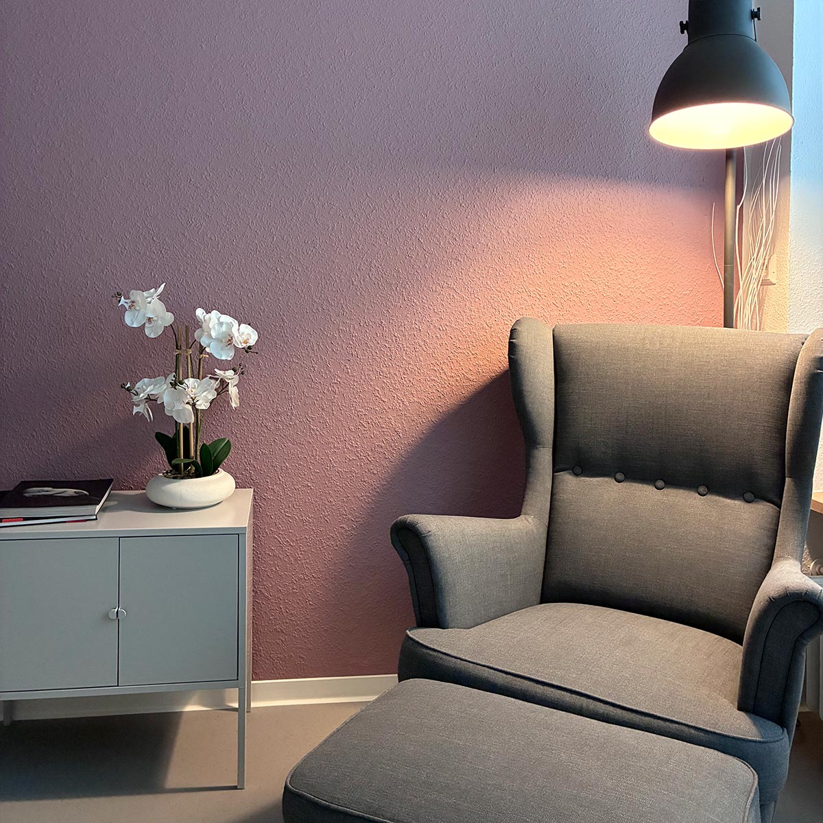 Gemütlicher Sessel mit Lampe neben einer Anrichte mit Blumen